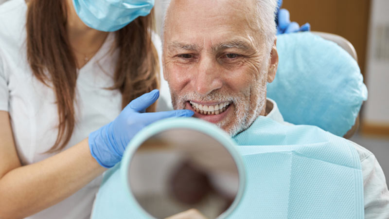 Paziente uomo sorridente si guarda allo specchio dal dentista